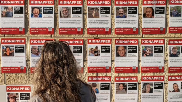 Eine Frau steht vor einer Wand mit „Kidnapped“-Plakaten der Hamas-Geiseln.