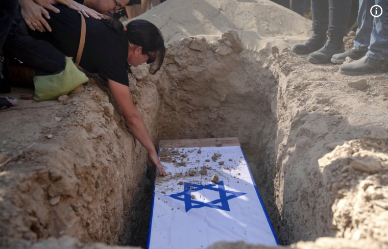 Eine Frau beugt sich über einen Sarg mit israelischer Flagge, der in ein Grab gesenkt wird.