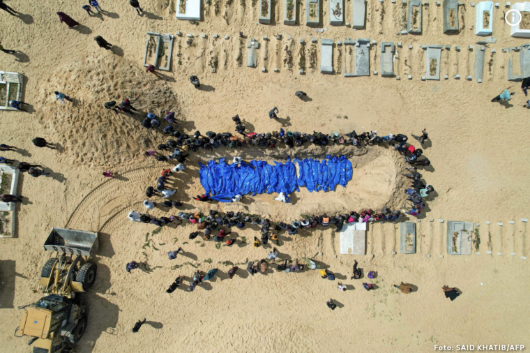 Luftaufnahme eines Massengrabs in Gaza: in blaue Tücher gehüllte Leichen, umringt von Menschen.